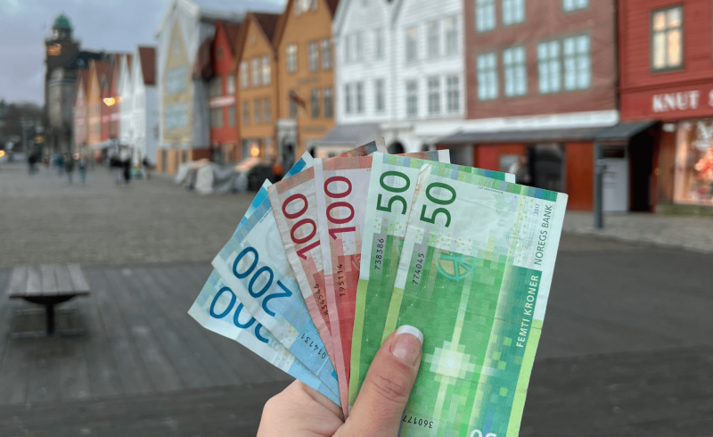 Foto segurando coroas norueguesas na frente de Bryggen. Arquivo pessoal