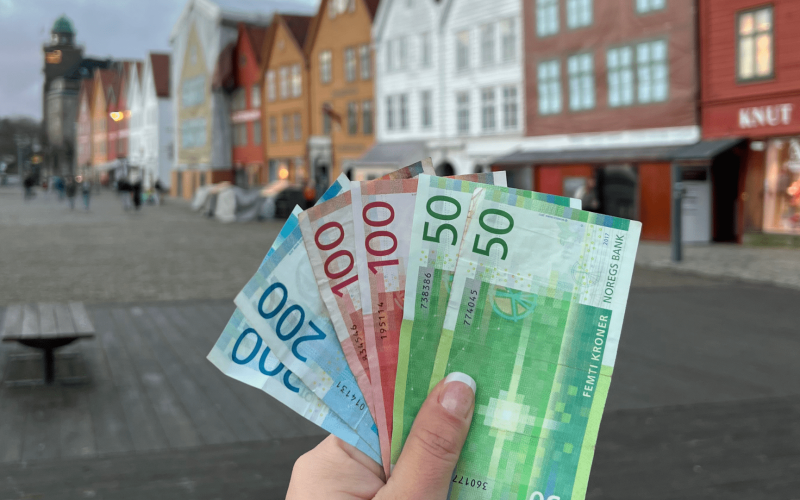 Foto segurando coroas norueguesas na frente de Bryggen. Arquivo pessoal